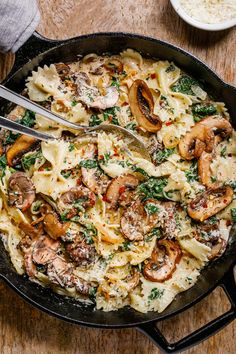 a skillet with pasta, mushrooms and parmesan cheese in it on a wooden table