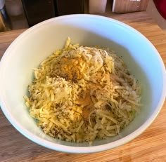 a white bowl filled with shredded cheese on top of a wooden table next to a knife