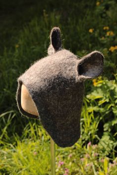 a brown bear hat sitting on top of a wooden pole next to flowers and grass