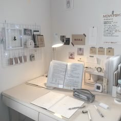 a white desk topped with an open book next to a lamp and other office supplies