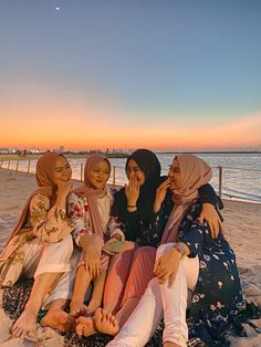 four women sitting on the beach at sunset