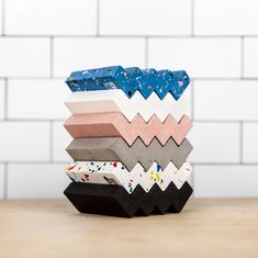 a stack of different colored papers on top of a wooden table next to a white brick wall