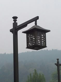 a lamp post with a bird feeder on it's side in front of some trees