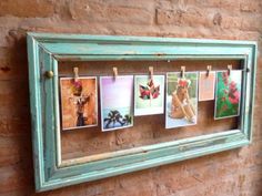 an old wooden frame with photos hanging on clothes pins in front of a brick wall