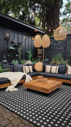 an outdoor living room with black and white rugs, wooden furniture and hanging lights