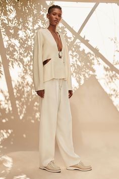 a woman standing in front of a tree wearing white pants and a blazer jacket