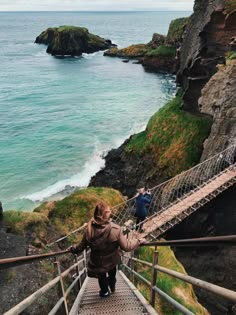 two people walking up stairs to the ocean with cliffs in the background and water on either side