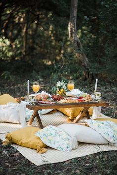 a picnic table with food and drinks on it in the middle of a forest filled with trees