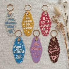 six keychains with different designs on them sitting next to some dried plants and flowers