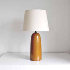 an orange ceramic table lamp with a white shade on the top, sitting on a white surface