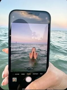 someone holding up their cell phone to take a photo of them in the water with an ocean background