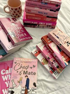 a pile of books sitting on top of a bed next to a cup and saucer