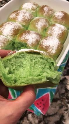 a person holding up a green dessert in front of a white dish filled with powdered sugar