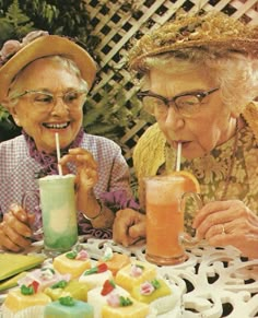 two older women sitting at a table with drinks in front of them, one drinking from a cup and the other holding a straw