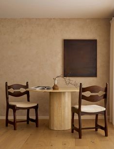 two wooden chairs sitting at a table in front of a painting hanging on the wall