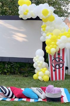 an outdoor movie party with popcorn, balloons and blankets on the grass in front of a large screen