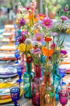 colorful vases filled with flowers sit on a table set for an outdoor dinner party