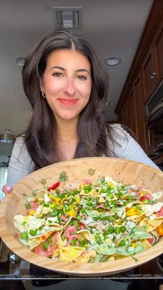 a woman holding up a large wooden bowl filled with vegetables and vegtables