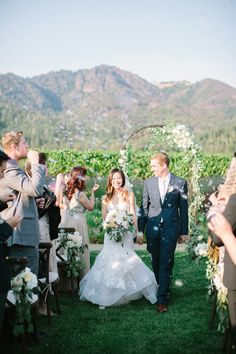 a bride and groom walking down the aisle after their wedding ceremony in front of mountains