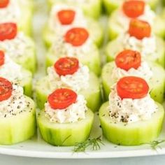 small cucumbers with tomatoes and cream cheese on them are arranged on a white platter