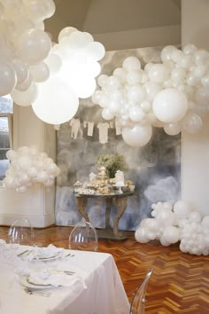 balloons are hanging from the ceiling in front of a table with white tables and chairs