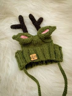 a knitted deer hat with antlers on it's head is laying on a white fur surface