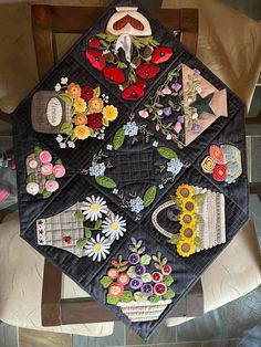 a quilted table top with flowers and vases on it sitting on a chair