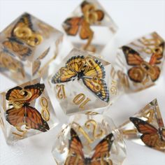 six clear dice with gold butterflies and numbers on the sides, sitting on a white surface