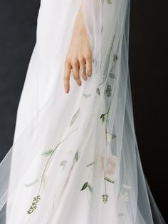 a close up of a person wearing a wedding dress with flowers on the skirt and veil