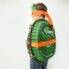 a young boy is wearing a green and orange turtle costume with an orange band around his head