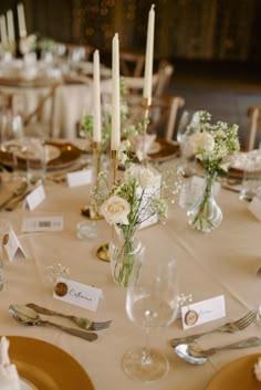 the table is set with place cards, silverware and flowers in glass vases