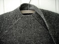 a gray sweater hanging on a white wall with a wooden hanger in front of it