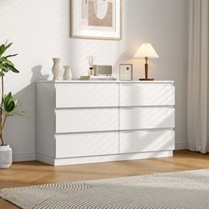 a white dresser sitting on top of a hard wood floor next to a potted plant