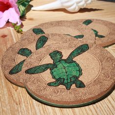 two coasters with green turtles on them sitting on a table next to pink flowers