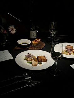 two white plates topped with food next to a glass of wine