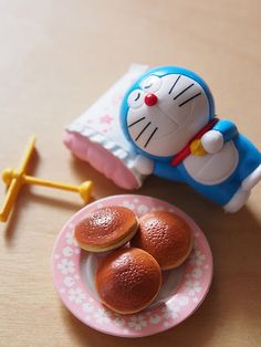 a toy cat sitting on top of a pink plate next to two donut holes