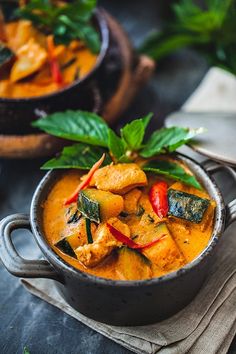 two bowls filled with curry and vegetables on top of a table next to green leaves