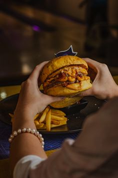 a person holding up a sandwich and french fries on a black plate in front of them