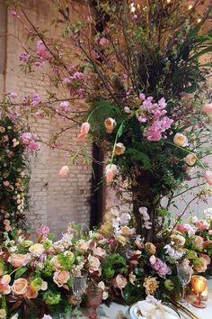 an arrangement of flowers and greenery on a table in a room with brick walls