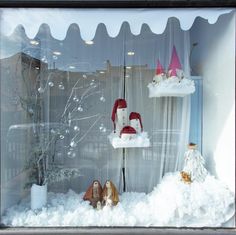 a window display with snow and gnomes in the front, behind which is a white curtain