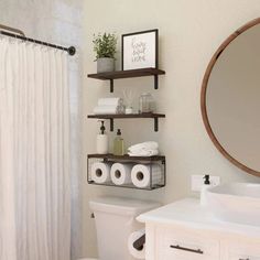 a white toilet sitting under a bathroom mirror next to a sink and a shower curtain