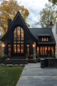 a black house with large windows and steps leading up to the front door is lit by lanterns