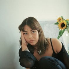 a woman sitting on the floor with her hand near her face and looking at the camera