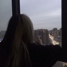 a woman is looking out the window at city lights and skyscrapers in the distance