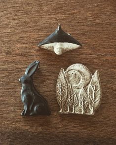 two small metal animals sitting next to each other on a wooden table with an ornament in the shape of a rabbit