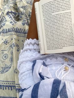 an open book sitting on top of a bed next to a blue and white blanket