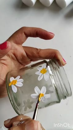 a woman is painting daisies on a mason jar