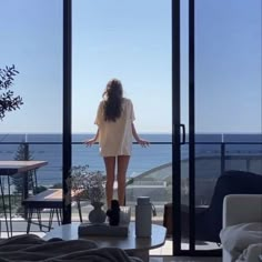 a woman standing in front of a window looking out at the ocean from inside a house