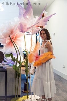 a woman standing next to a vase with flowers in it and holding an orange umbrella