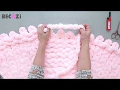 someone is crocheting a pink blanket with scissors and other crafting supplies on the table